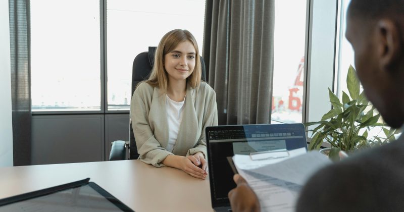 Woman sitting at a desk during a job interview. She is smiling