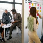 Two side by side images of a workplace. On the left side a group of people are having a meeting at a table. On the right side, two people are planning/writing information on a white board.