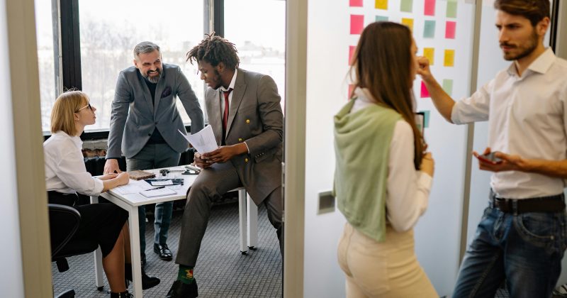 Two side by side images of a workplace. On the left side a group of people are having a meeting at a table. On the right side, two people are planning/writing information on a white board.