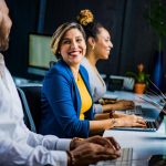 Woman in the work place on laptop smiling at colleague.