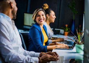 Woman in the work place on laptop smiling at colleague.