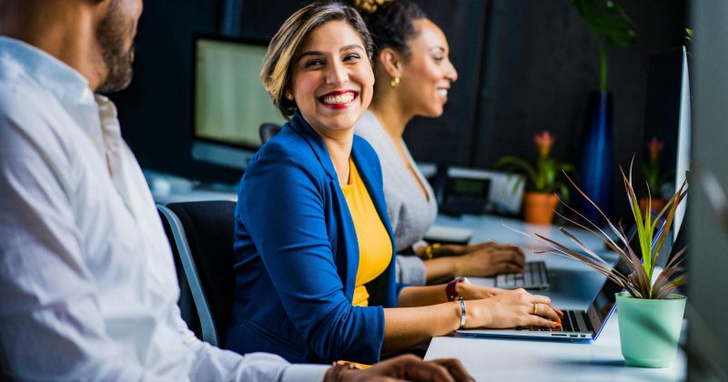 Woman in the work place on laptop smiling at colleague.