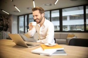 Man drinking a hot drink smiling at his desk.