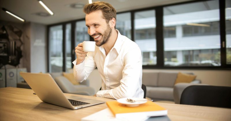 Man drinking a hot drink smiling at his desk.